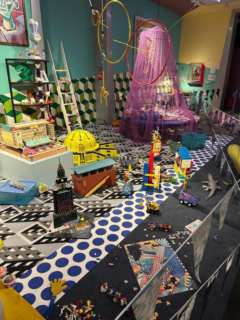 foto stella dekker Welcome to the dreamhouse
Dwaal door een levensgroot droomhuis in het Groninger Museum. Alle ruimtes – van de woonkamer en de slaapkamer tot de tuin – staan in deze tentoonstelling vol met postmodern design uit de eigen collectie van het museum. Een haast filmische wereld komt tot leven waarin details, contrasten, kleuren en humor centraal staan. Van rondslingerend speelgoed tot gebruikte asbakken – de kamers ademen het dagelijks leven en spelen met de imperfectie die echte interieurs kenmerkt.
Het Groninger Museum beschikt over de grootste museale collectie postmodern design in het land, opgebouwd sinds de jaren tachtig onder leiding van voormalig directeur Frans Haks. In Welcome to the Dreamhouse! is werk te zien van invloedrijke ontwerpers als Alessandro Mendini, Ettore Sottsass en andere leden van de Memphis-groep, waaronder Michele de Lucchi, Masanori Umeda, George Sowden en Nathalie du Pasquier. Ook is er aandacht voor Philippe Starck, ontwerper van een van de paviljoens van het museum, en voor ontwerpers als Studio Job, Maarten Baas en Jaime Hayon, die elk op hun eigen manier het postmodernisme een nieuwe invulling geven.
De tentoonstelling is vormgegeven door Marloes en Wikke, gerenommeerde scenografen voor theater en opera, die met hun onconventionele stijl zorgen voor een speelse en theatrale presentatie.
Het Groninger Museum
2025
Ontwerp en Samenstelling
Marloes en Wikke
Conservator
Ruud Schenk
Lichtontwerp
Yuri Schreuders
Geluidsontwerp
Daan Hofman
Styling assistent
Juliette Mout
Grafische vormgeving
Rudo Menge
Hoofd collectie
Marieke van Loenhout
Stage M\\W
Menno Meijners
Peter Duel